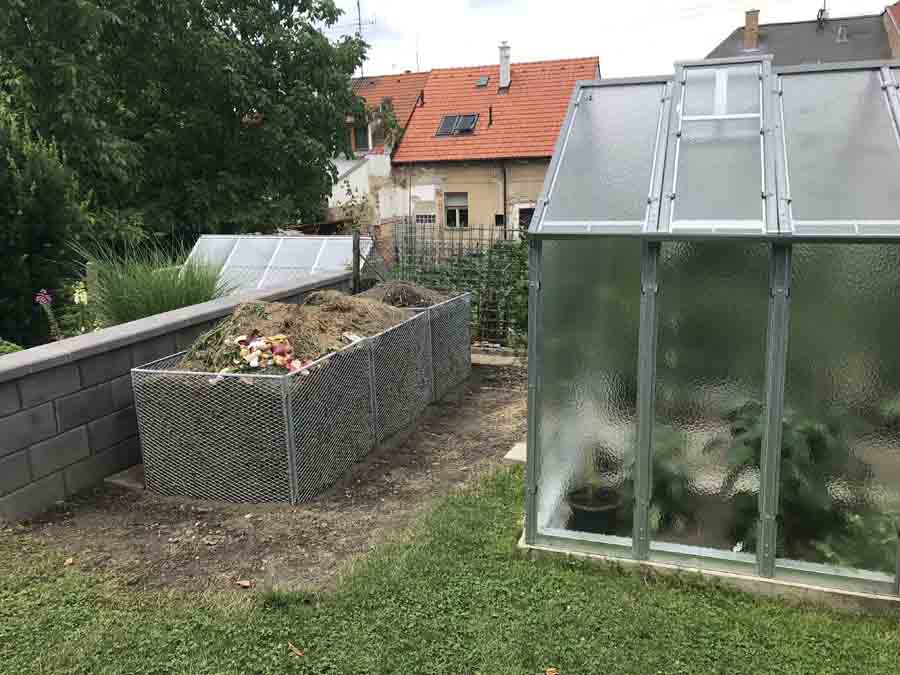 Pohled z dálky na kompostér naplněný kompostem vedle skleníku v zahradě | Kompostér na zahradní kompost | radyzezivota.cz