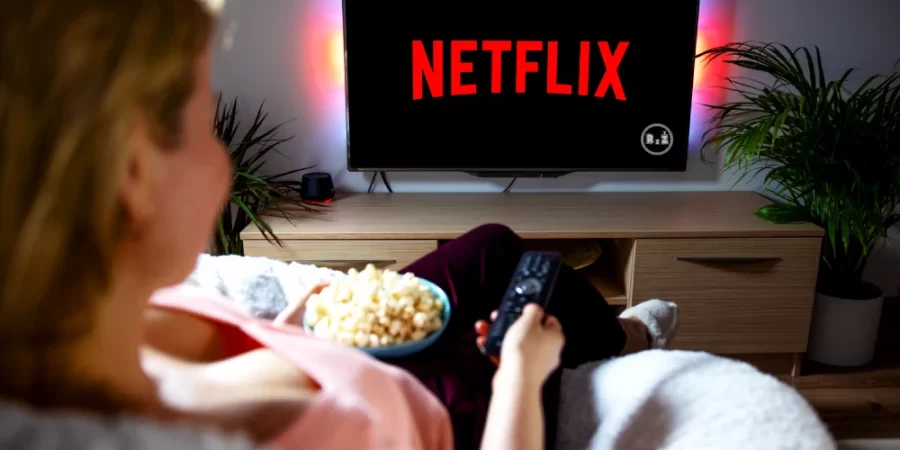Žena sedící pohodlně na gauči u televize s černým obrazem a červeným názvem NETFLIX držící v ruce ovladač v obyváku | Pro článek - TOP 20 nejlepších filmů pro dospělé na Netflixu | pro web: radyzezivota.cz | zdroj: shutterstock.com