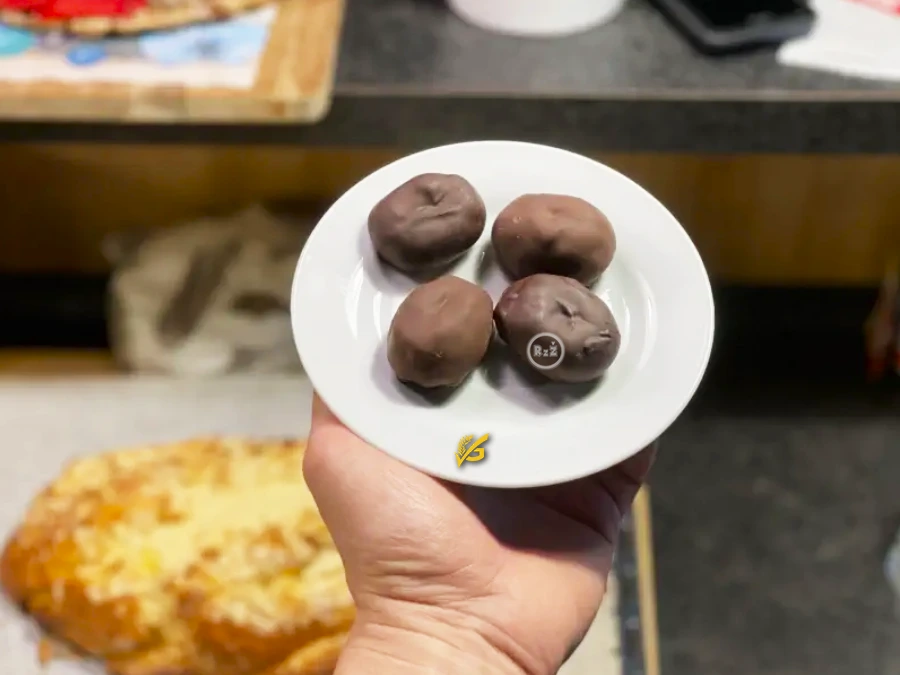 Bezlepková kávová zrna s čokoládou a marcipánem na bílém talířku drženém v ruce v pozadí kuchyně v vánočkou, adventním věncem se svíčkami a barem | Bezlepkové recepty | radyzezivota.cz | Pro článek: Bezlepkové kávové zrno | Autor fotografie: Jiří Samuel