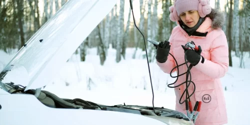 Žena stojící v zimě před svým automobilem držící v ruce startovací kabely připojující k autobaterii nevědíc postup jak na to | Pro web: radyzezivota.cz | Pro článek: Jak nastartovat auto s vybitou baterií | Zdroj: shutterstock.com