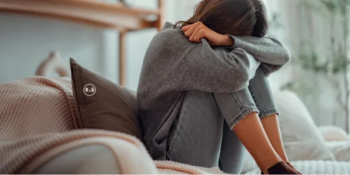 Mladá žena sedící na gauči v obyvacím pokoji schoulená do klubíčka se svěšenou hlavou držící se kolem sebe staženými nohami opírající se o polštář přičemž jeji obličej není vidět neboť jej má opřený k nohám - prochází složitou situaci | Pro článek: Mohou antidepresiva pomoci? 2.článek - Jak na depresi | Pro web: radyzezivota.cz (Rady ze života) | Zdroj: shutterstock.com