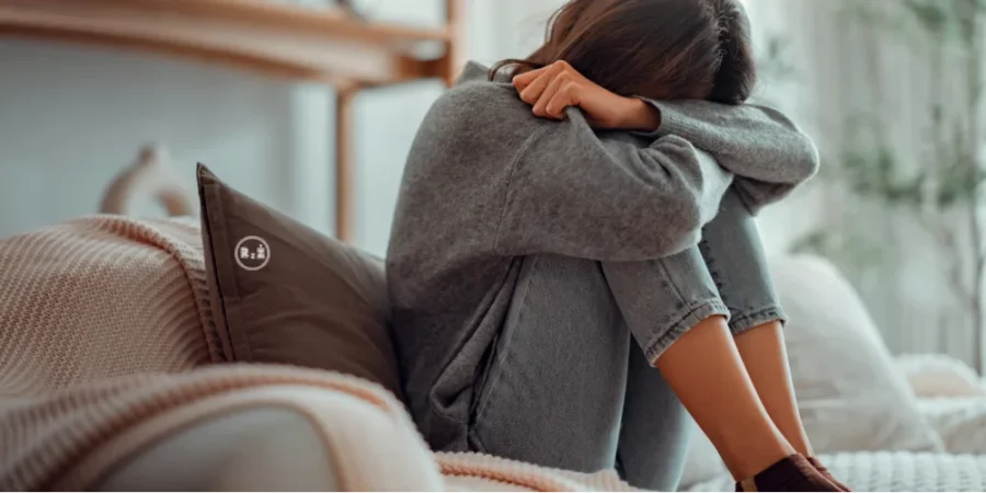 Mladá žena sedící na gauči v obyvacím pokoji schoulená do klubíčka se svěšenou hlavou držící se kolem sebe staženými nohami opírající se o polštář přičemž jeji obličej není vidět neboť jej má opřený k nohám - prochází složitou situaci | Pro článek: Mohou antidepresiva pomoci? 2.článek - Jak na depresi | Pro web: radyzezivota.cz (Rady ze života) | Zdroj: shutterstock.com
