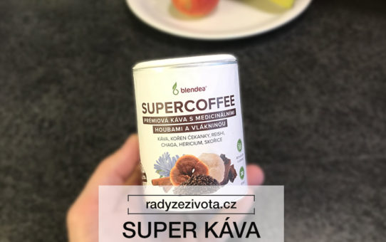 Fotografie instantní kávy SUPERCOFFEE v papírové nádobě držena v ruce v pozadí kuchyňská linka a talíř s ovocem