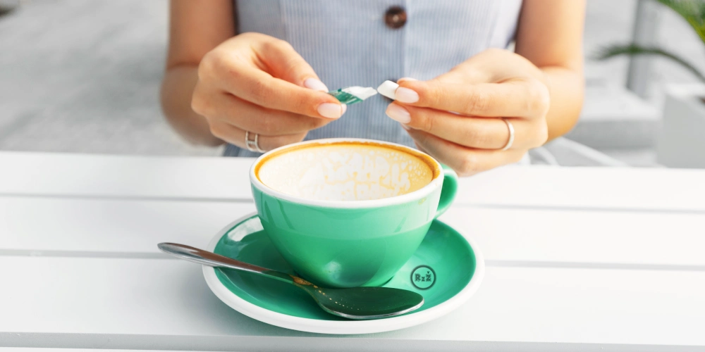 Na obrázku sedící žena u stolu držící v rukou žvýkačku nad stolem s vypitou kávou | Pro článek: Vysoký krevní tlak