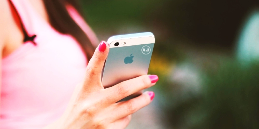 Fotografie ženy držící v ruce iPhone od společnosti Apple s růžově nalakovanými nehty s růžovou halenkou s rozmazaným pozadím zelené přírody | pro článek - Iphone není intuitivní | pro web: Rady ze života (radyzezivota) | zdroj: pixabay, Image by a Jan Vašeka from